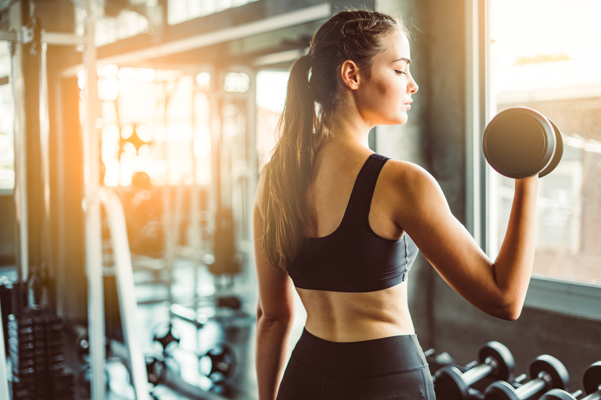 Young girl playing dumbbell to exercise in fitness.Slim girl lifts heavy dumbbell while training in the gym. Sports concept fat burning and a healthy lifestyle.